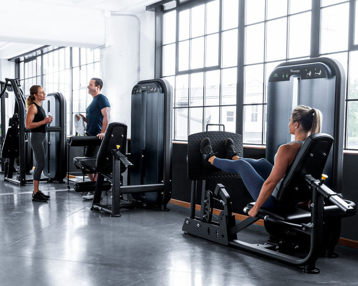 vision fitness lifestyle image - females and male in gym setting - leg press