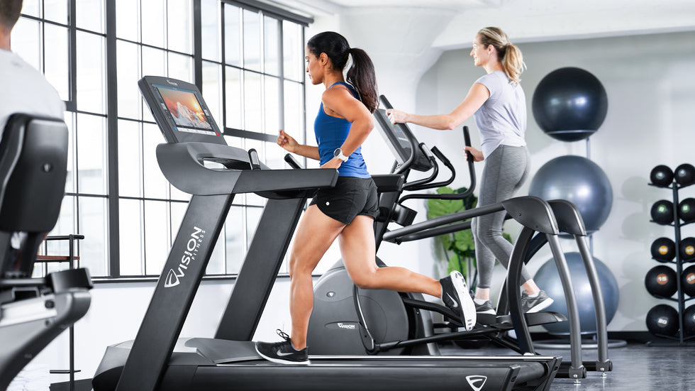 Lady in Short and Blue Top running on Vision Fitness Treadmill in Gym Space - lifestyle image - woman on elliptical background
