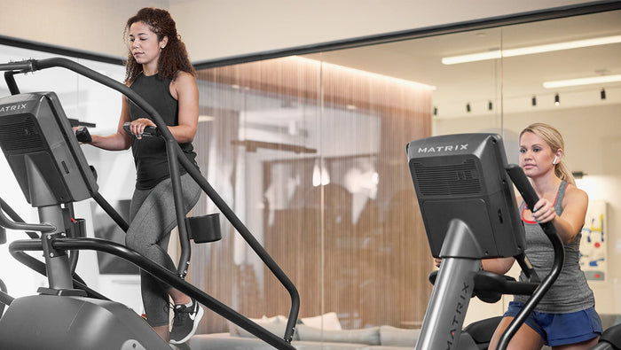two females matrix elliptical and climbmill - gym indoor setting